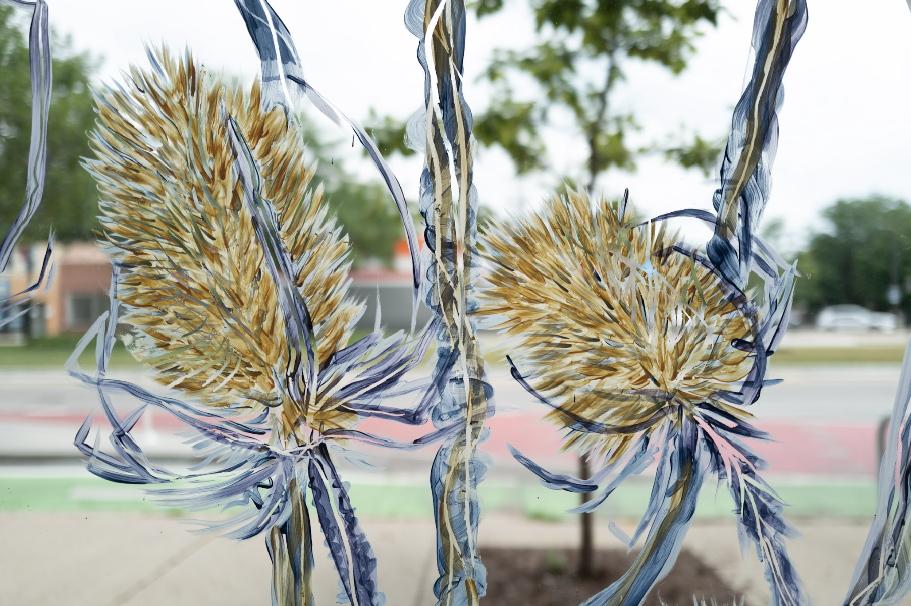 Close view of blue, gold, cream, and lavender botanical forms painted directly onto the gallery storefront glass, with Clark Street visible beyond.