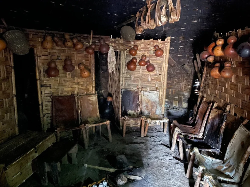 A hut interior furnished with animal skin-covered chairs, gourds for cooking and carrying water