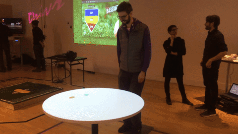 A man frantically runs around a table trying to lead projection of a snake to food.