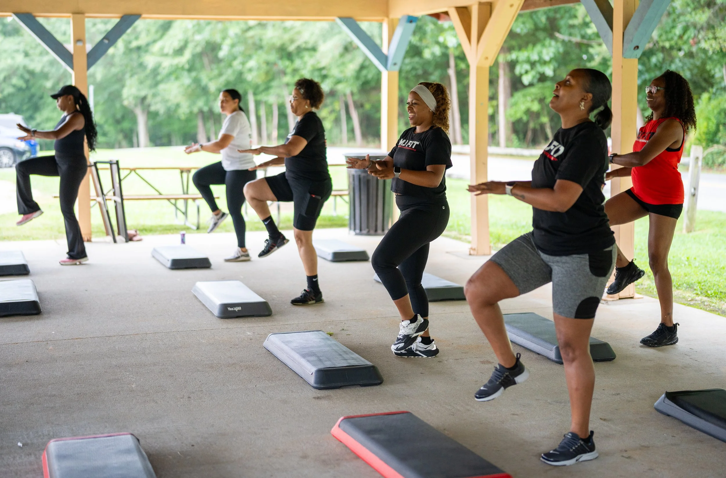 MJ Fit Training group participating in an outdoor step fitness class under a pavilion.