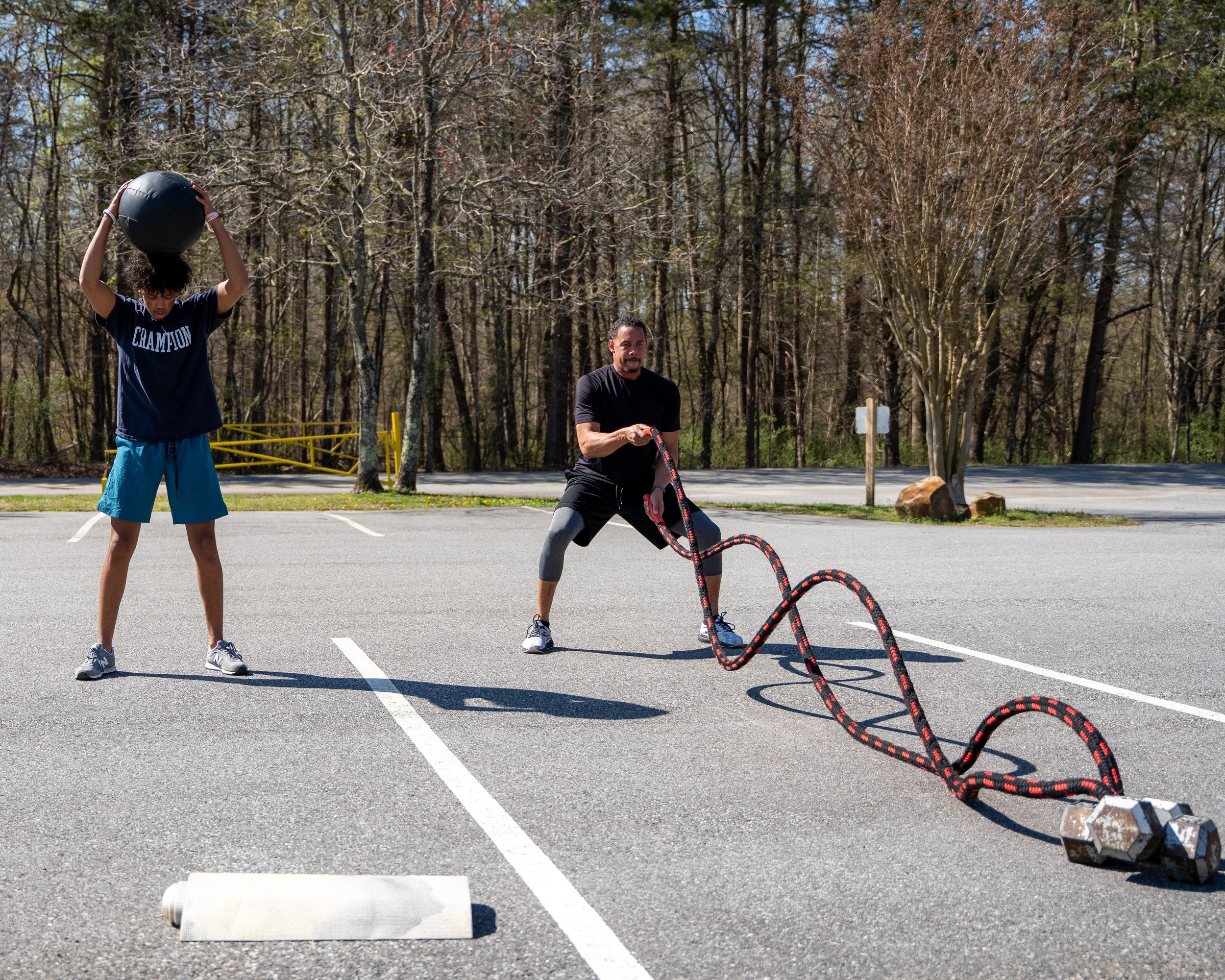 MJ Fit Training participants performing medicine ball and sledgehammer exercises during an outdoor circuit workout.