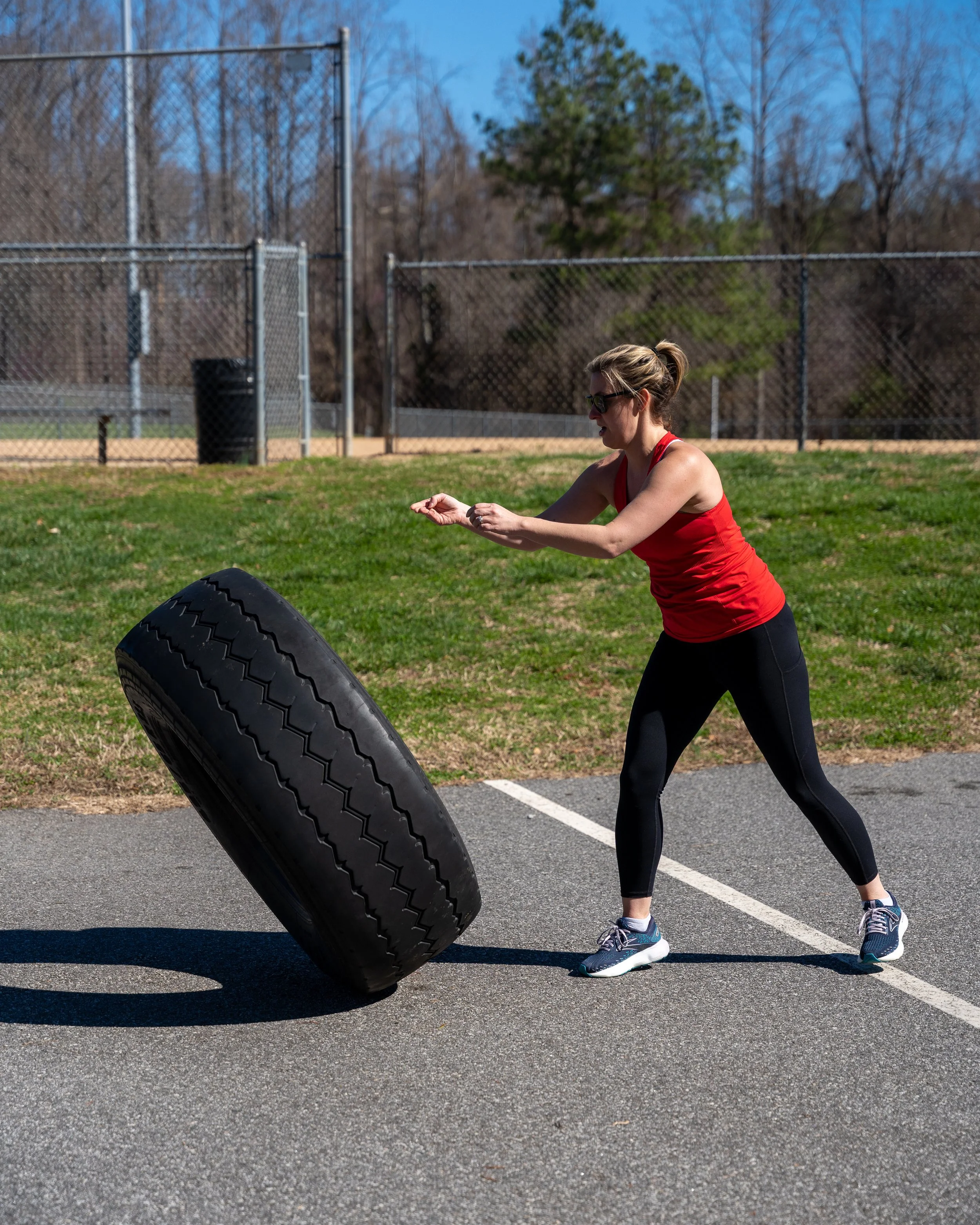 Woman performing a tire exercise during an outdoor MJ Fit Training workout.