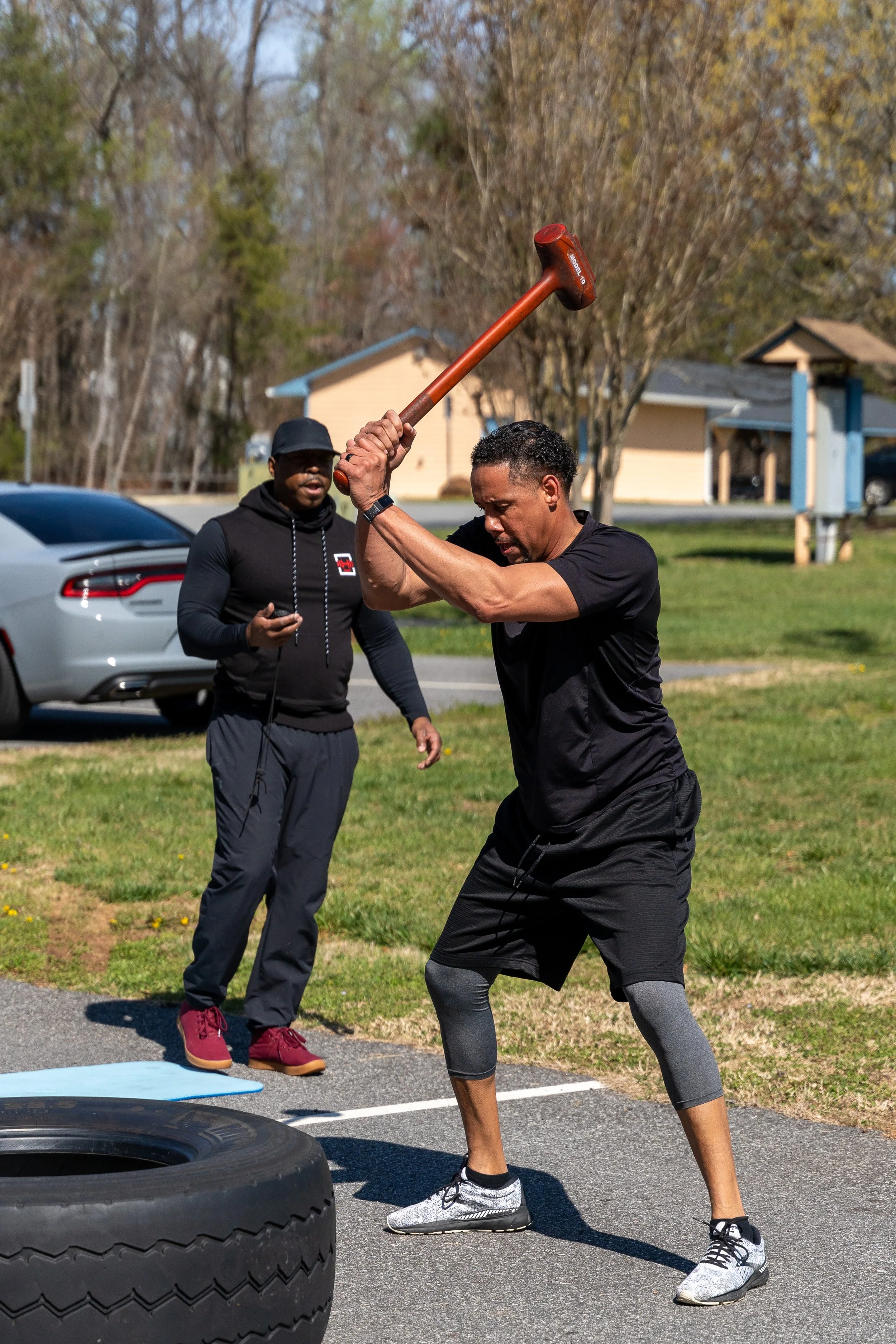 MJ Fit Training participant performing a sledgehammer exercise during an outdoor fitness workout.