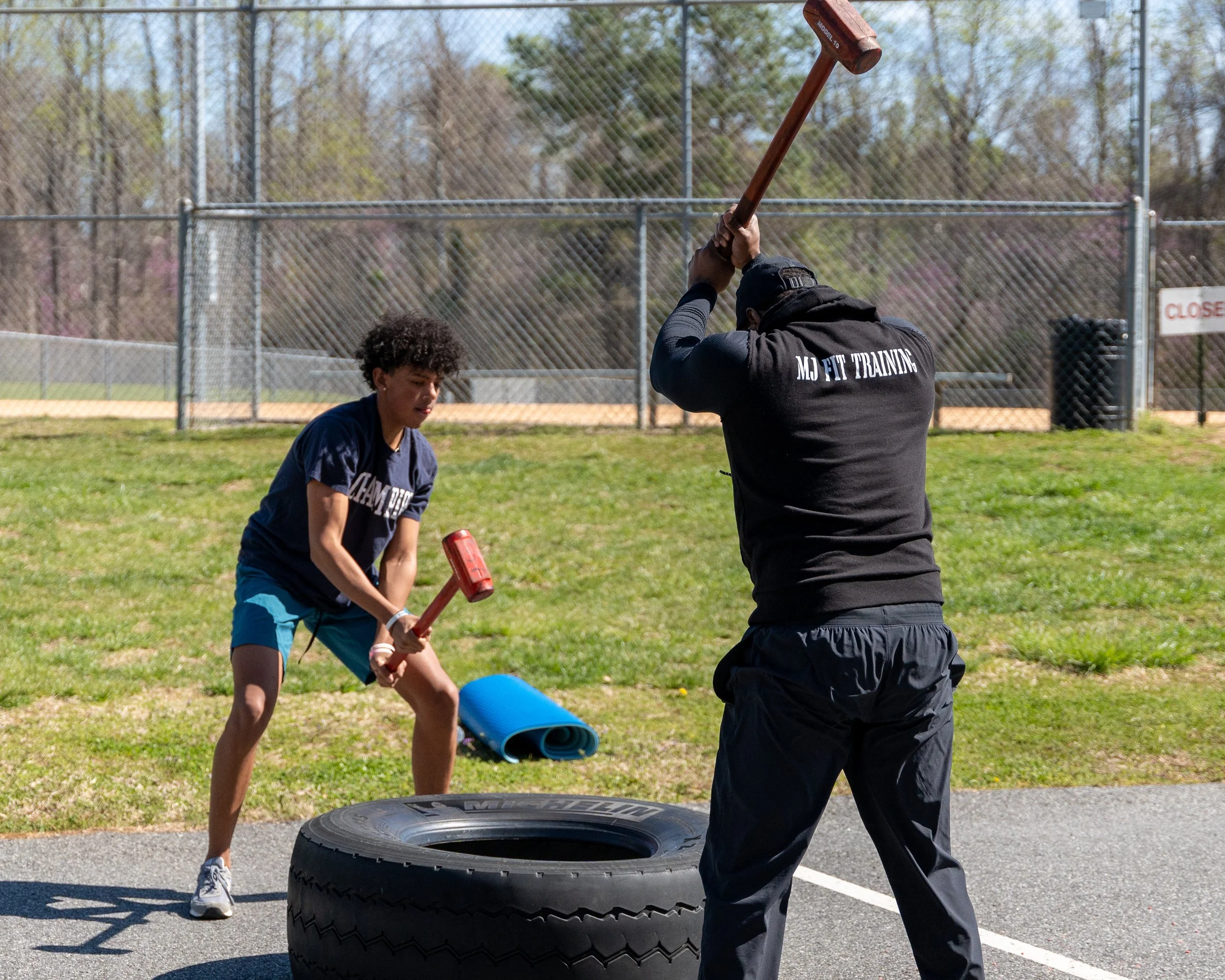 MJ Fit Training participants performing sledgehammer and tire exercises during an outdoor fitness workout.