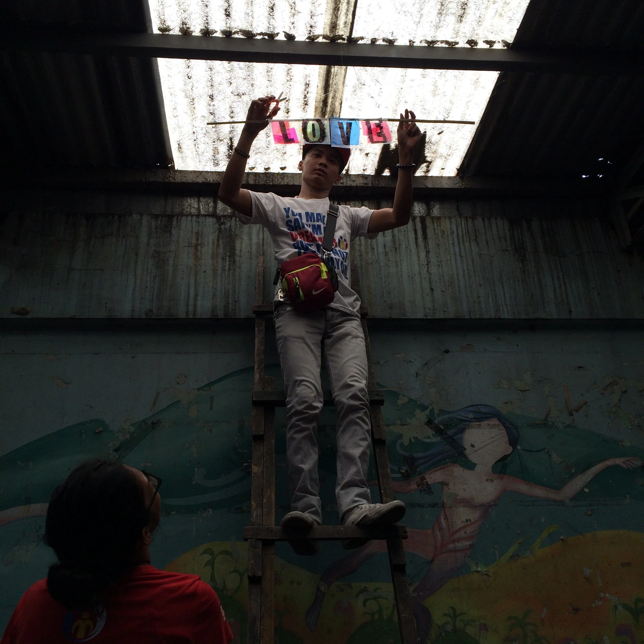  Illuminated Words, Tondo, Philippines, 2016  Wendell, a Project Pearls volunteer, hangs the first illuminated word,  Love . 
