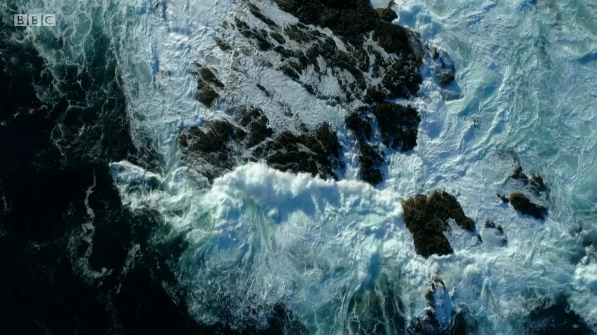 Top-down drone aerial of waves breaking over rocks in Cornwall for BBC Two's This Fishing Life