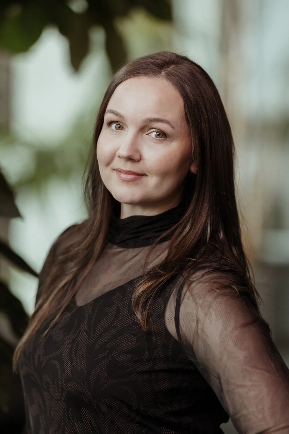 Nainen mustassa läpikuultavassa paidassa kasvien edessä ikkunoiden luona