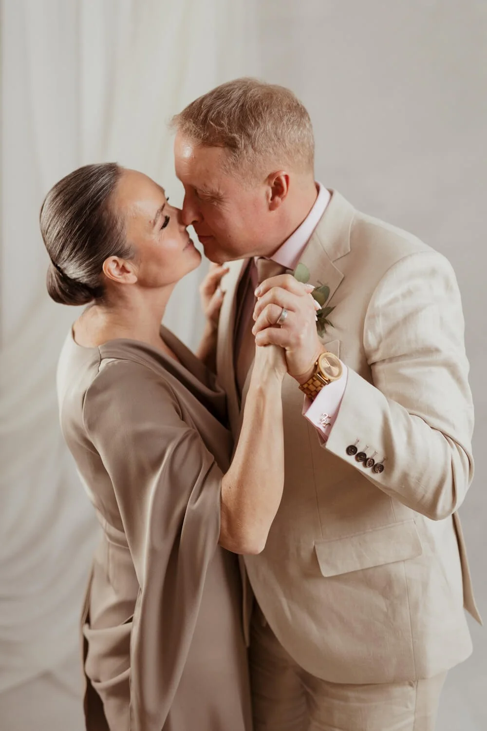 Hääpari tanssii studiossa beigeissä vaatteissa