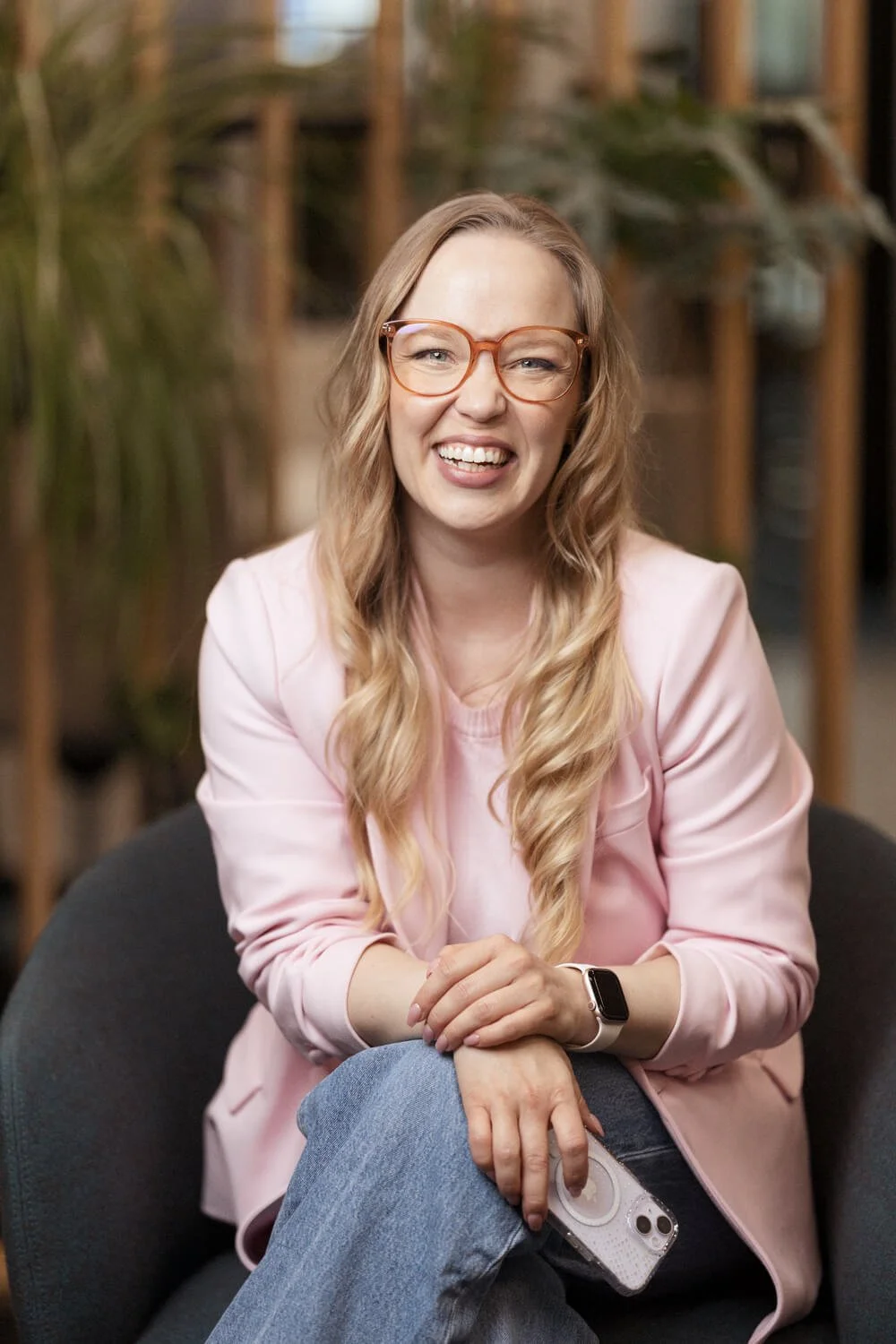 Nainen vaaleanpunaisessa jakussa nauraa kännykkä kädessä