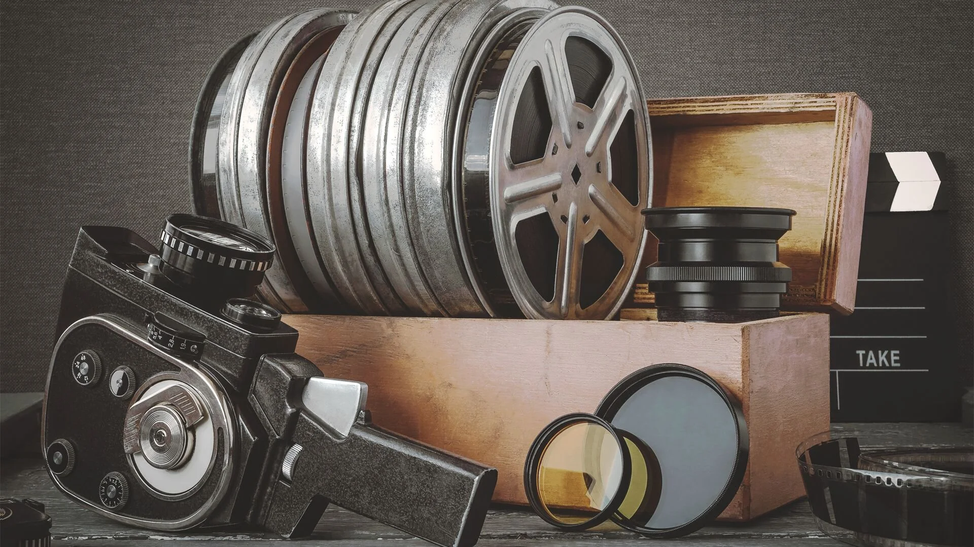 Collection of vintage film equipment including multiple film reels, a vintage camera with a lens, and various filters, with a wooden box and film clapperboard in the background.
