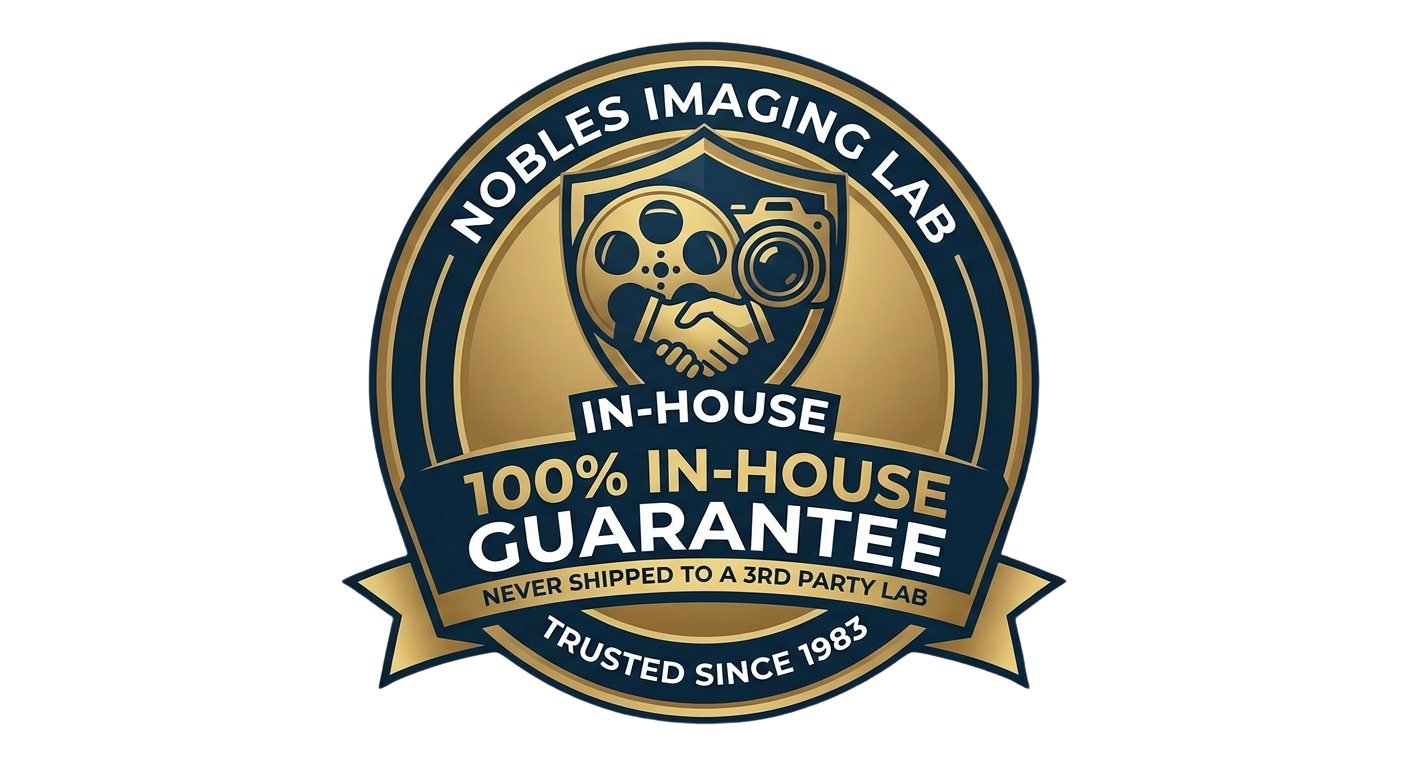 A circular badge with a gold and navy blue design, featuring a handshake, a film reel, and a camera. The text reads: 'Nobles Imaging Lab', 'In-House', '100% In-House Guarantee', 'Never Shipped to a 3rd Party Lab', and 'Trusted Since 1983'.