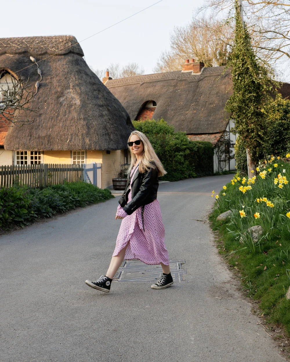 Woman crossing the road in English village wearing pink midi dress and black converse