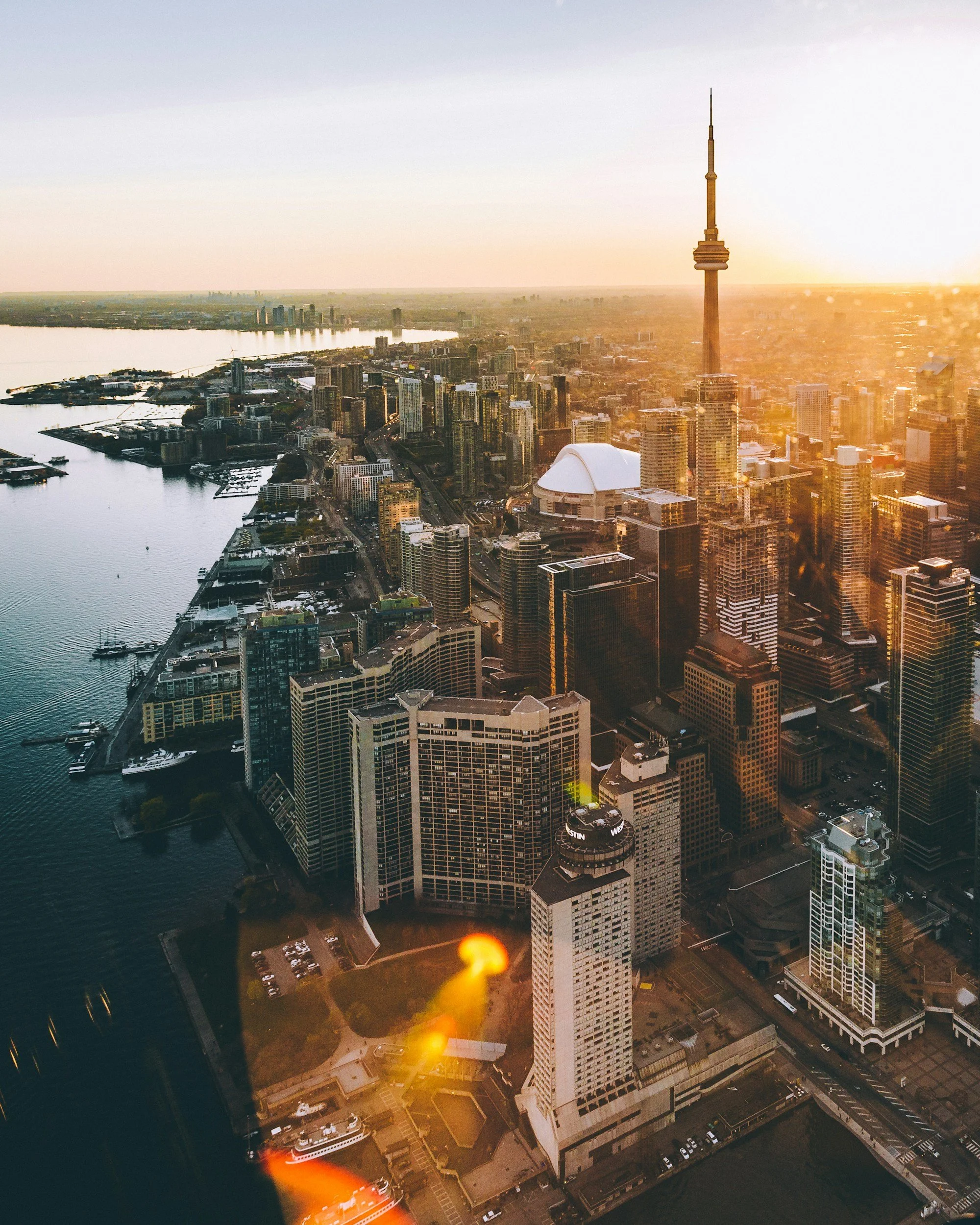 High-angle view of downtown Toronto, Canada during sunset, featuring the CN Tower, high-rise buildings, waterfront, and city streets.