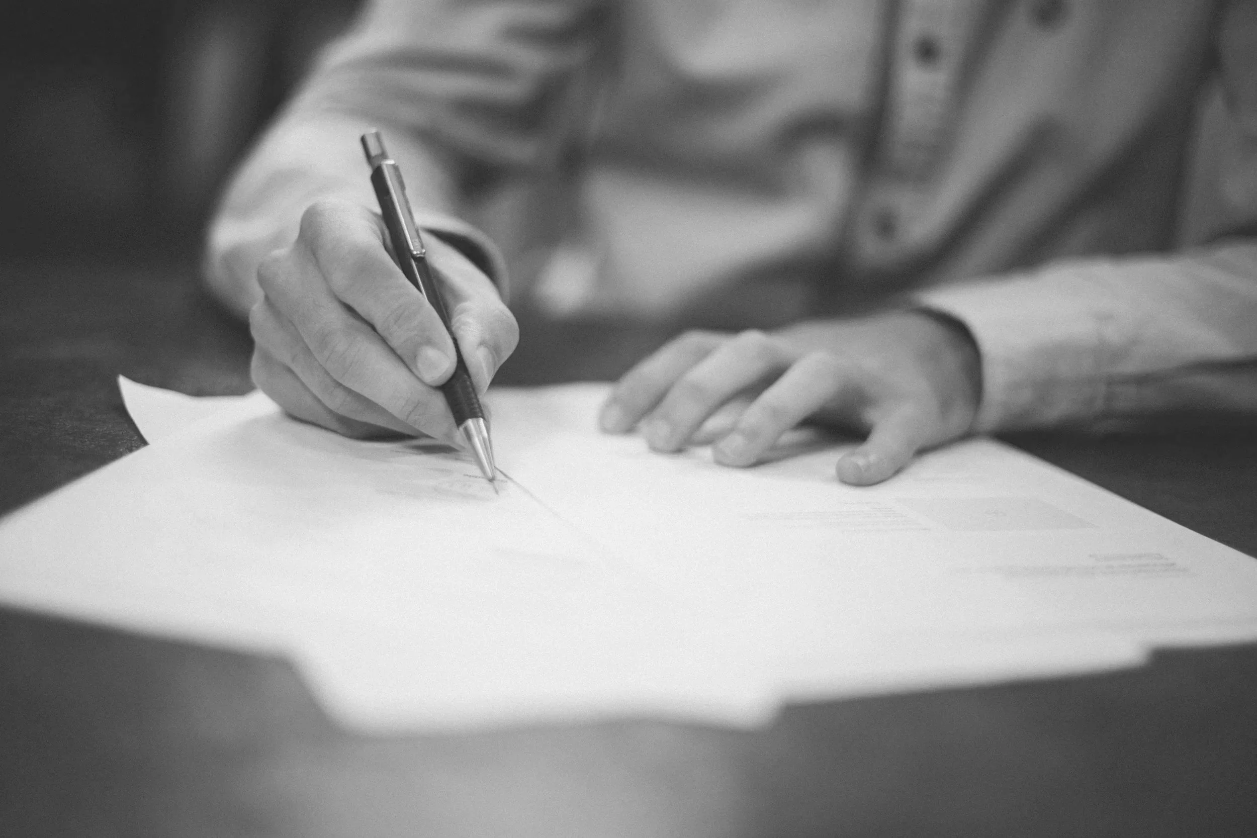 A person writing on a sheet of paper with a pen, with only their hand visible in the image.