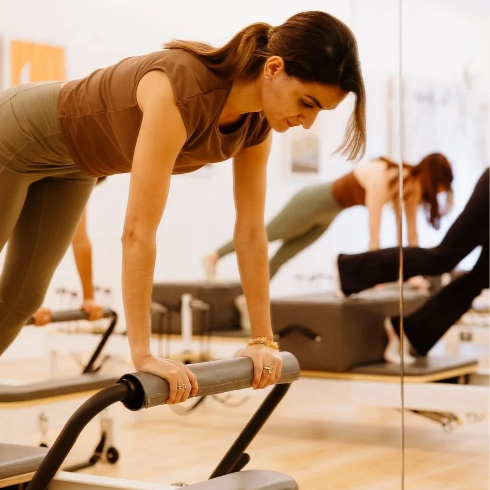 A Pilates participant practising on a reformer with hands on the footbar.