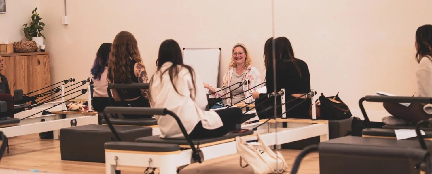 A teacher training group learning together around Pilates reformers.