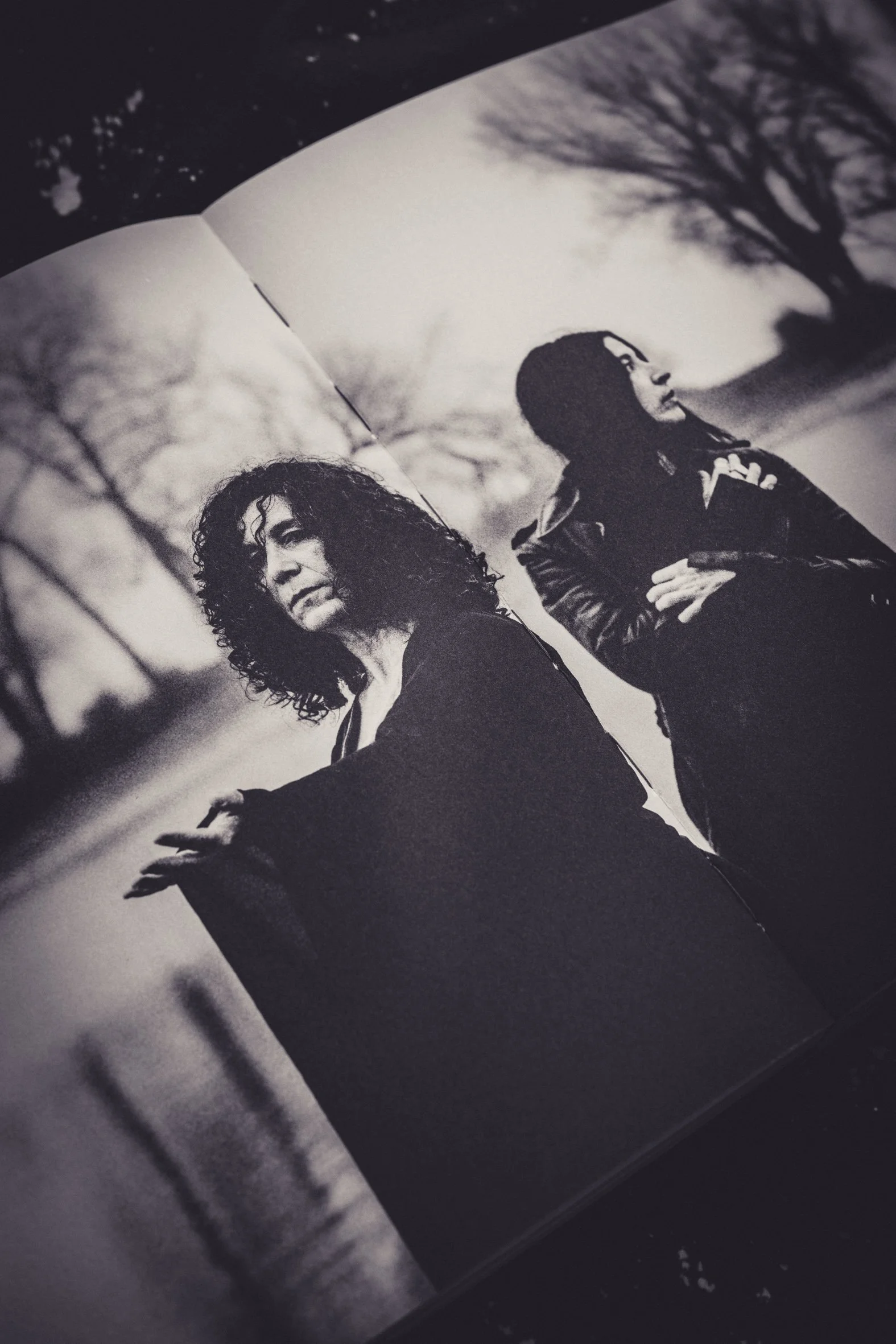 Schwarz-weiß-Fotografie von zwei Frauen, die im Freien stehen, mit Bäumen im Hintergrund, eine trägt eine Jacke mit Kapuze und die andere hat lockiges Haar.