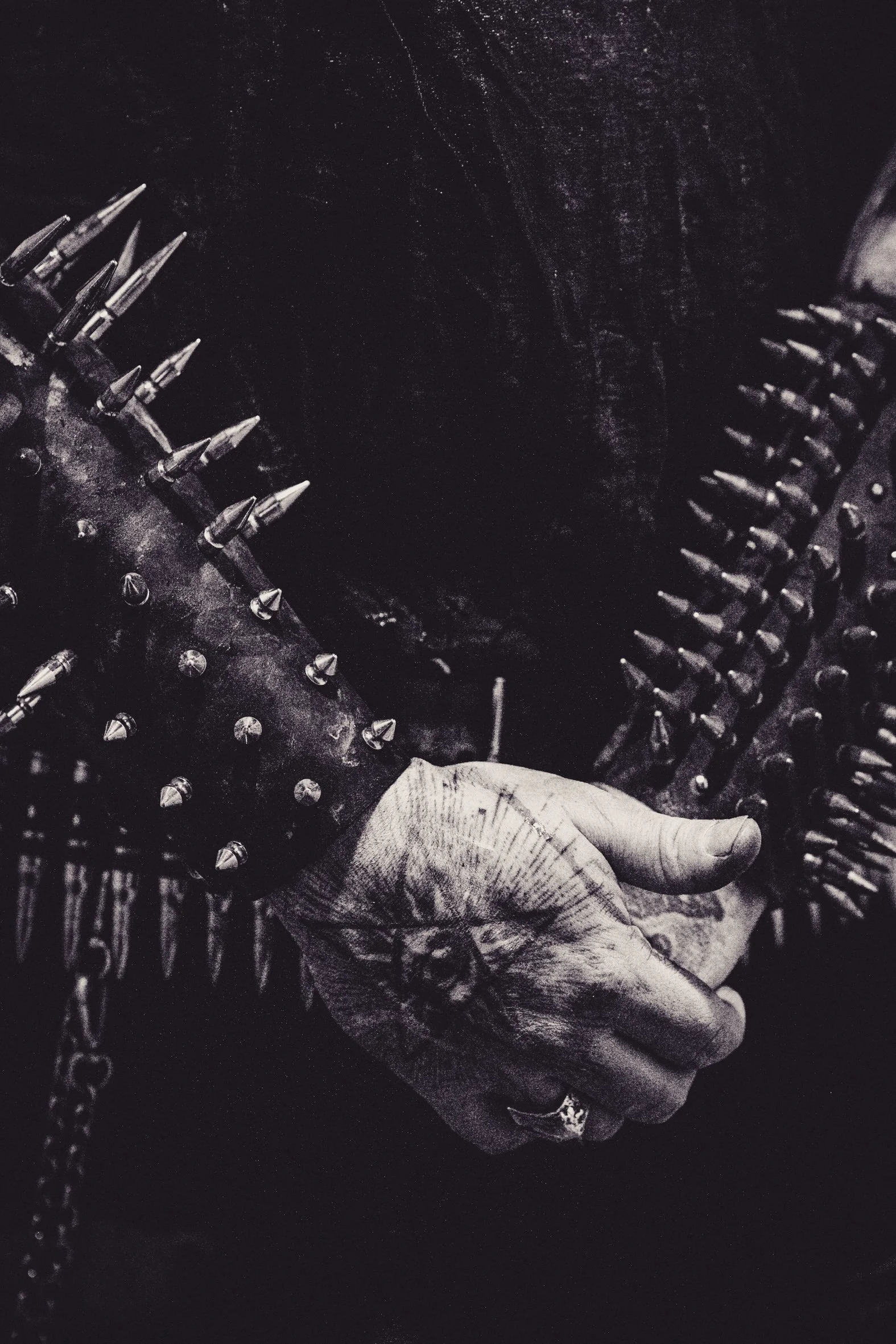 Schwarz-weiße Aufnahme einer Hand, die eine harte, spitze Nadel hält, umgeben von Nadelstreifen. Im Hintergrund sind metallene Nadeln oder Stifte sichtbar, die auf einer dunklen Oberfläche liegen.