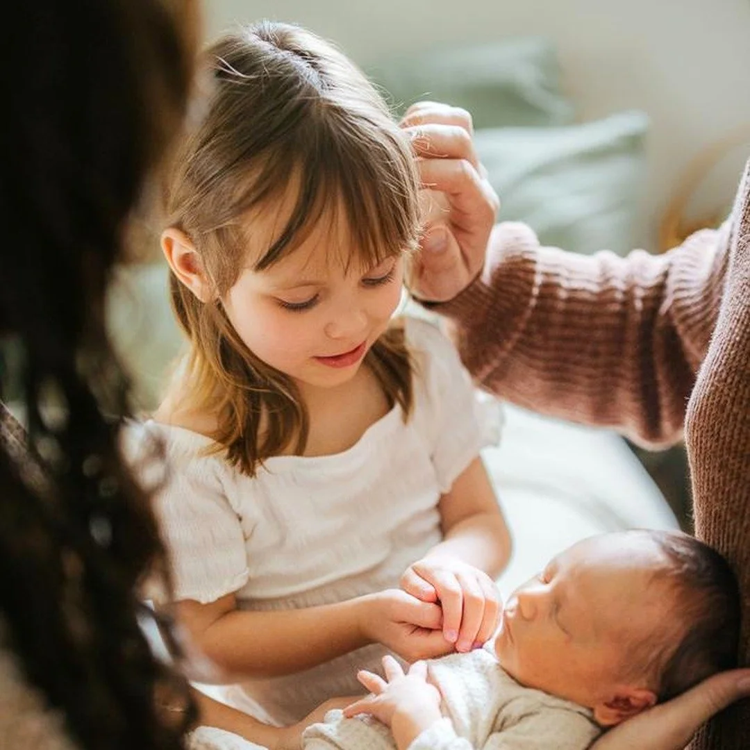 Sister looks down at newborn baby during an in home photoshoot in Durham NC