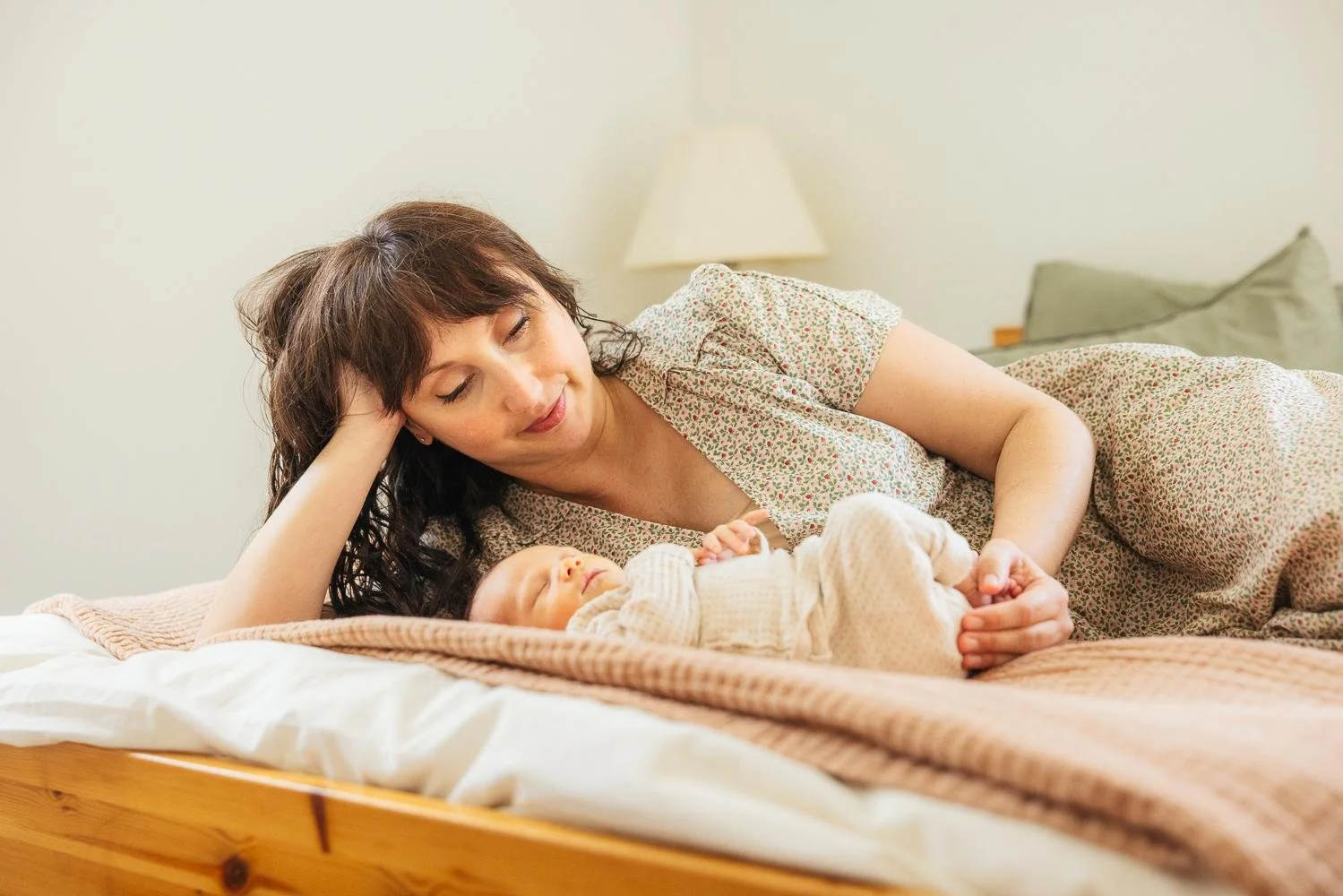 Mother lying on a bed gazing softly at her sleeping newborn baby during a Durham NC lifestyle newborn session