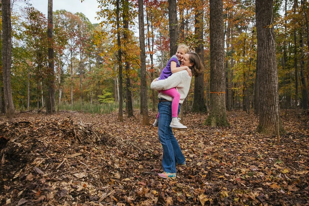 Mom holding young daughter while laughing in woods