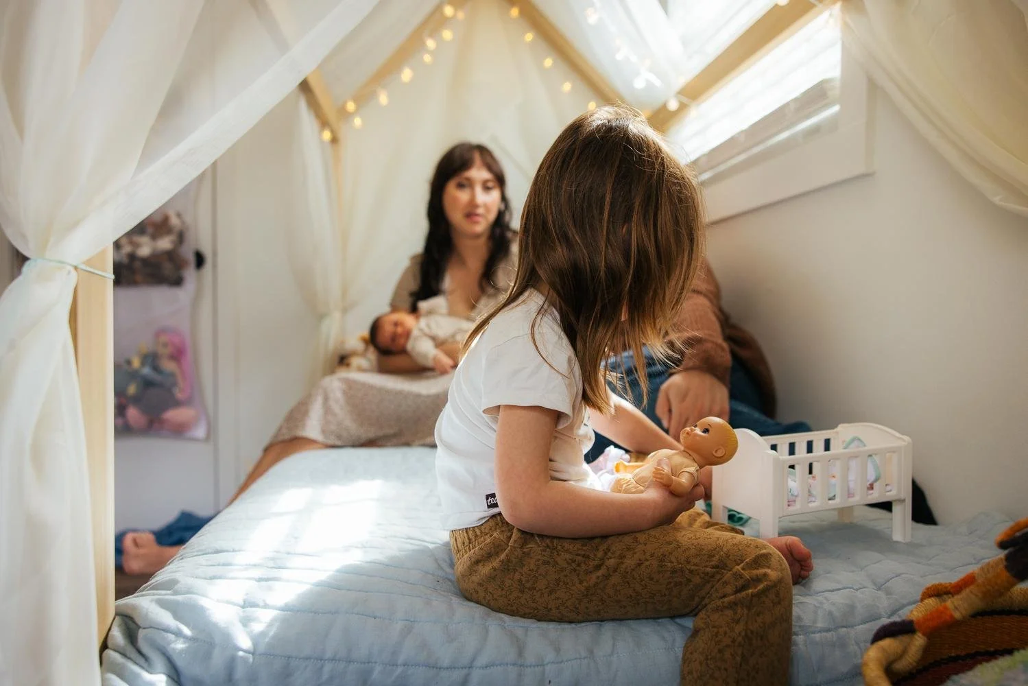 Toddler girl playing with toys inside a canopy tent while mom holds newborn in the background — Durham NC lifestyle newborn photography
