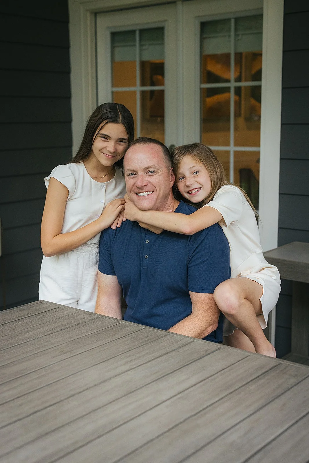 Dad and teenage daughters on back porch during in-home family photography session Chapel Hill NC