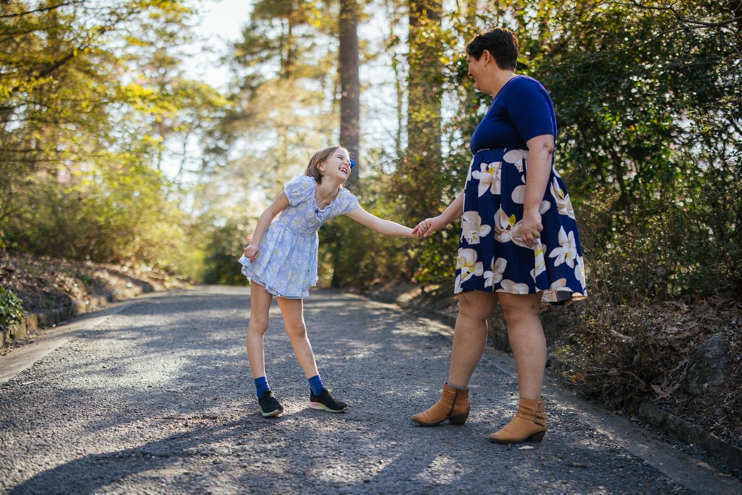 Mom and older daughter holding hands and dancing together on a garden path at Duke Gardens Durham North Carolina