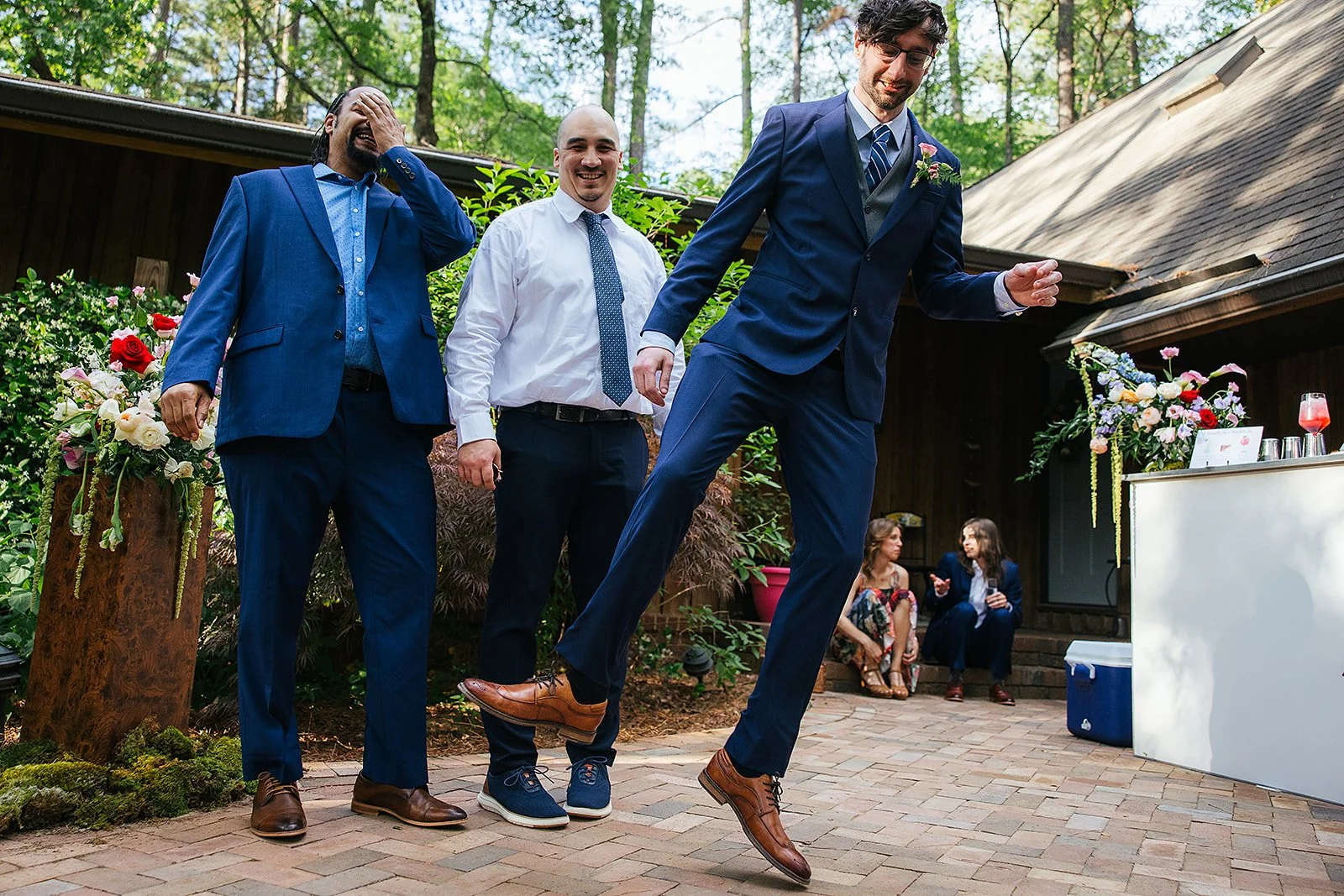 Groom leaps into the air with a huge smile while dancing at the outdoor wedding reception with guests and a bar setup in the background, Durham NC