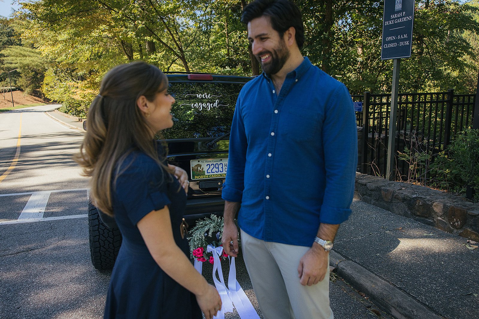 Couple in front of car with We're Engaged sign