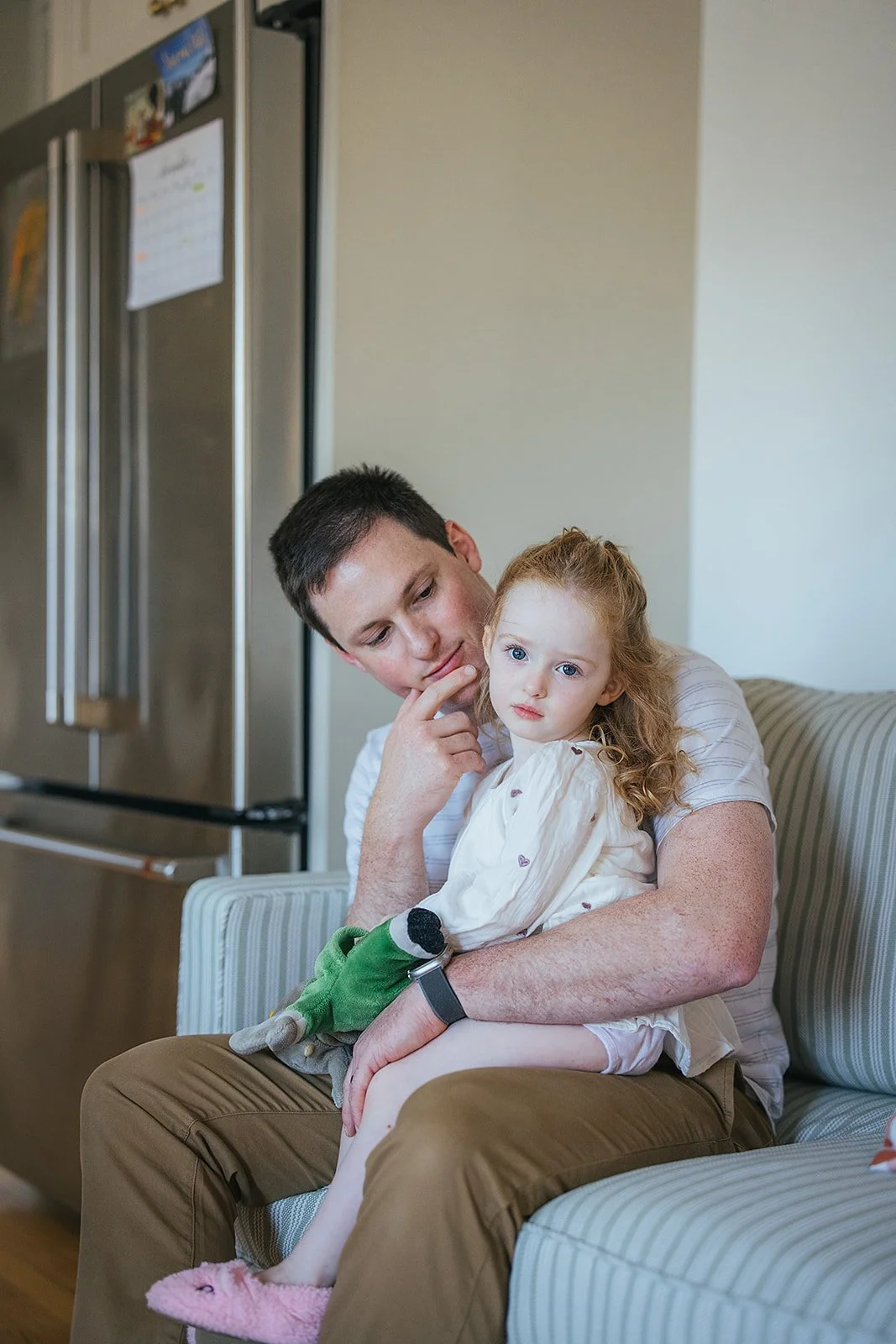 Dad and toddler daughter share a quiet tender moment on the couch during Durham in-home family photography session