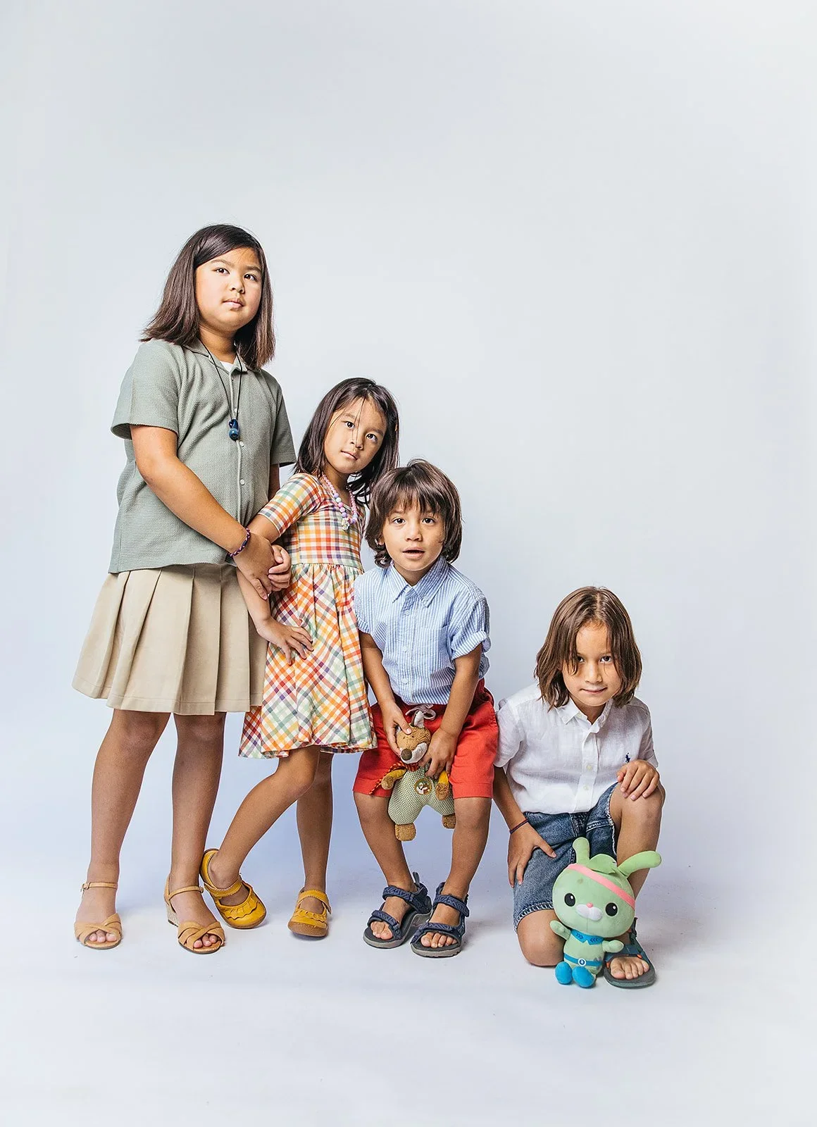 FourSiblingsStandingSideBySideInFrontWhiteWall.webp