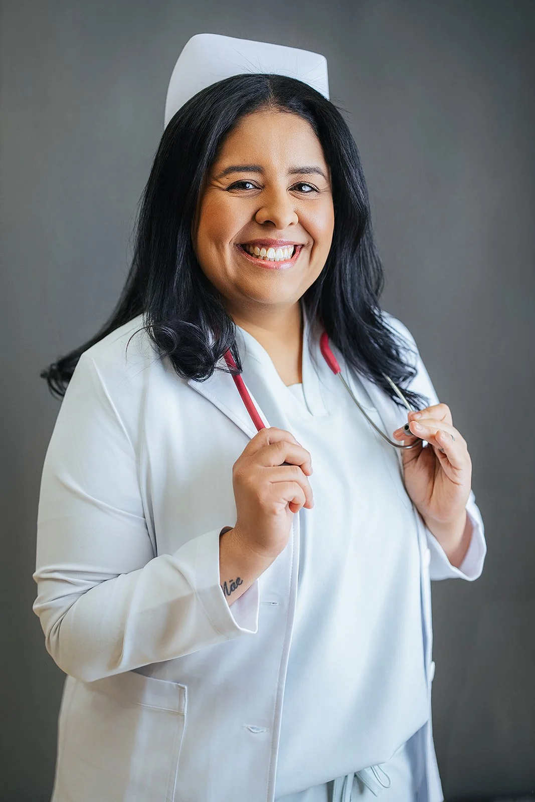 Durham Tech nursing student in white nurse cap and lab coat, holding red stethoscope with a joyful smile, professional headshot in Durham NC