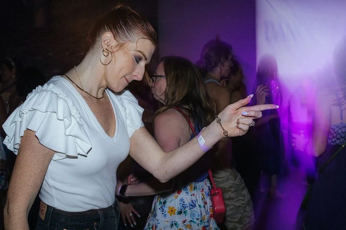 Woman in a white ruffled top moving to the music under purple lights at the Dance Her popup event, Raleigh NC