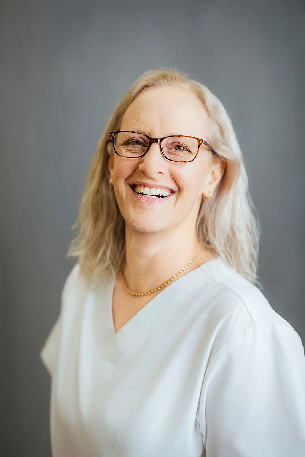 Durham Tech nursing student with platinum hair and tortoiseshell glasses, joyful laugh in white scrubs, professional nursing headshot in Durham NC