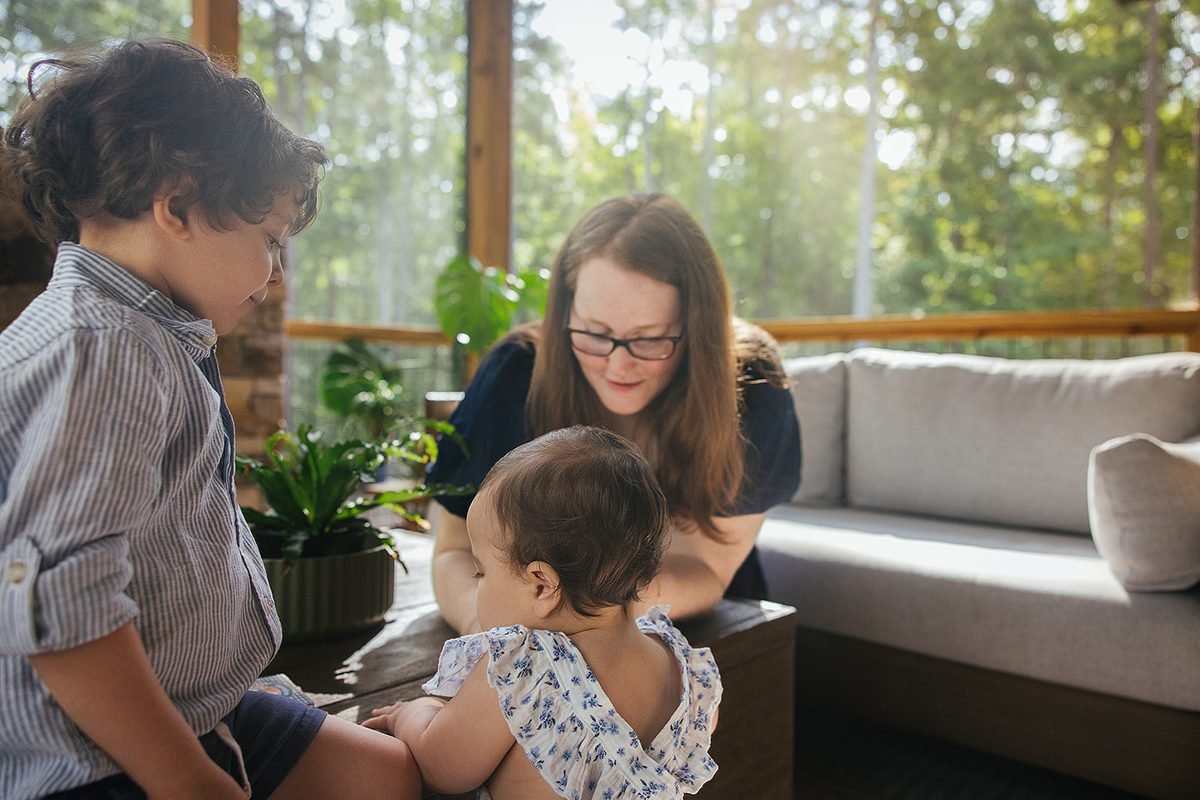 Mom playing with two young children while on screened in porch during in-home family photography session