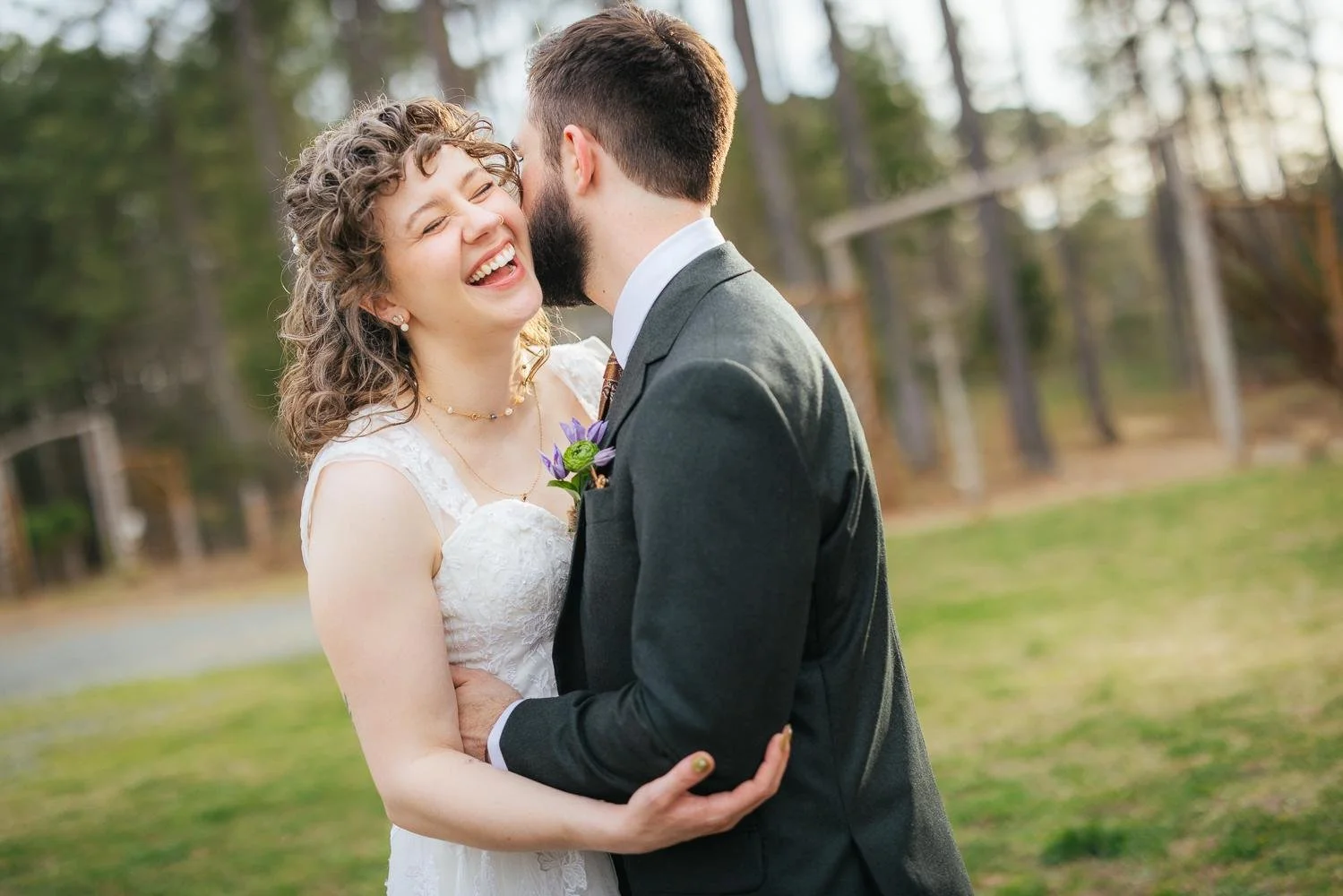Bride Emily laughing joyfully with eyes closed as groom Connor nuzzles her cheek among the pine trees at Honeysuckle Tea House Chapel Hill NC