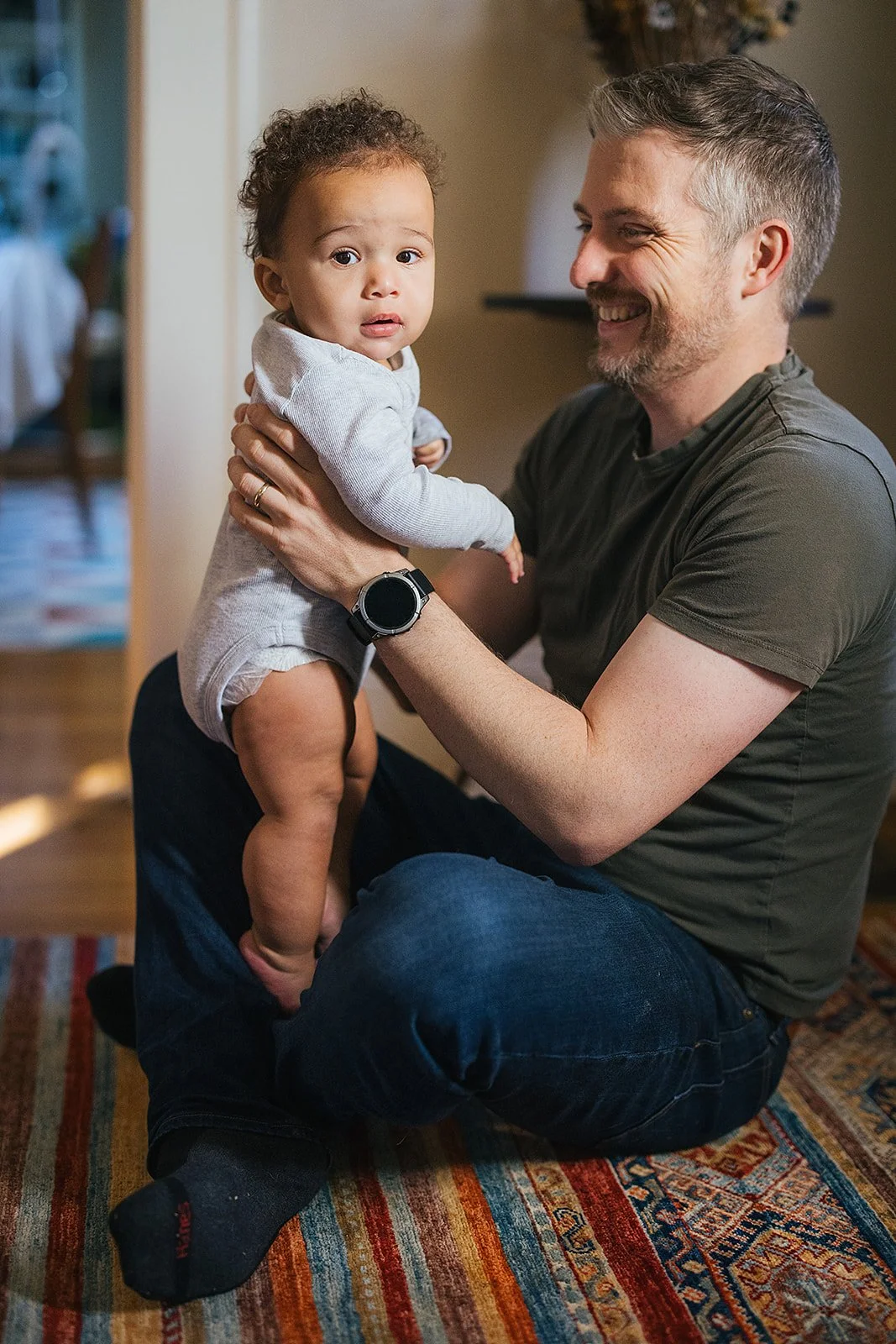 Dad Holding Young Child Sitting on Floor In Family Living Room