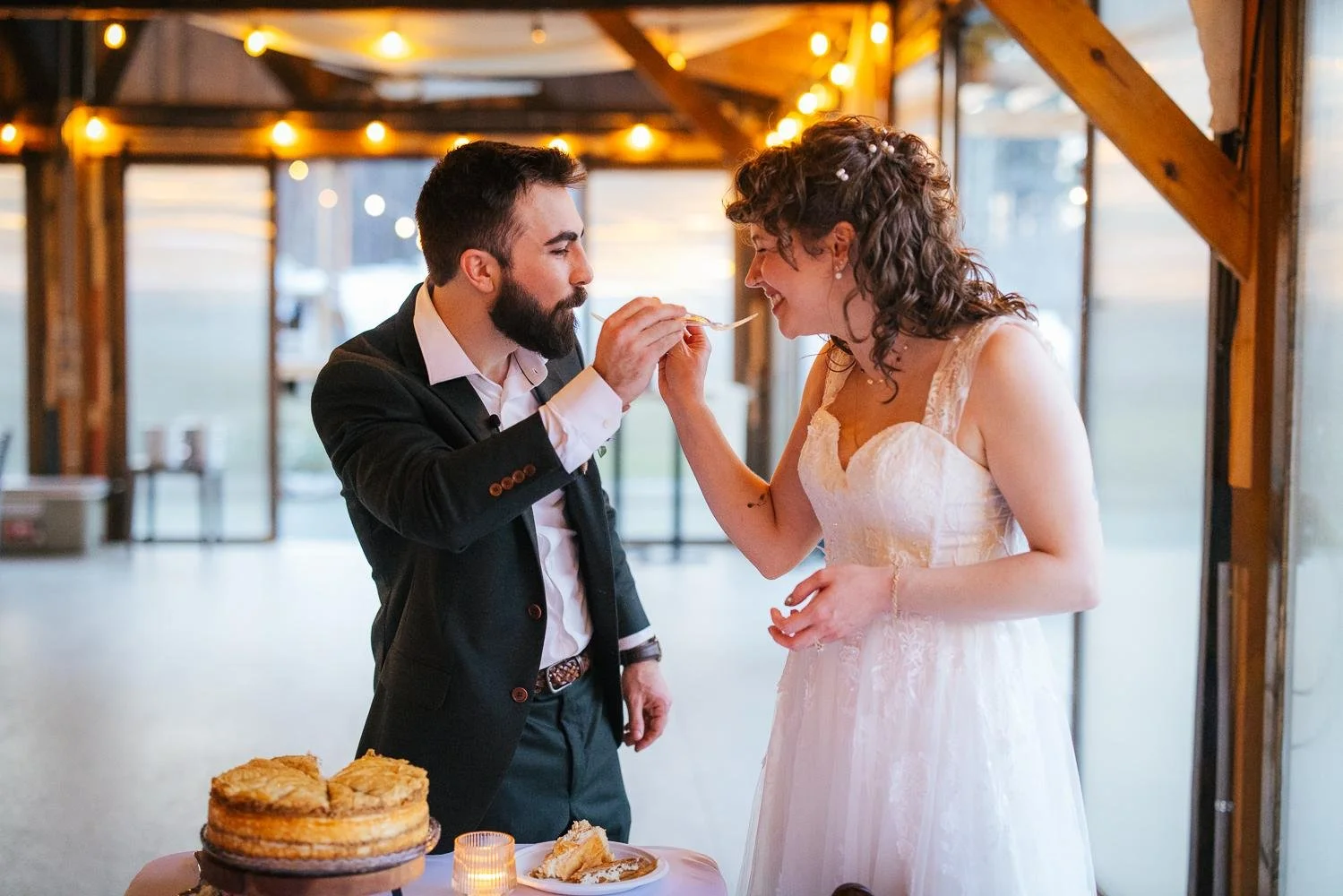 Bride and groom feeding each other pie during the pie cutting at the reception pavilion at Honeysuckle Tea House Chapel Hill NC — string lights overhead