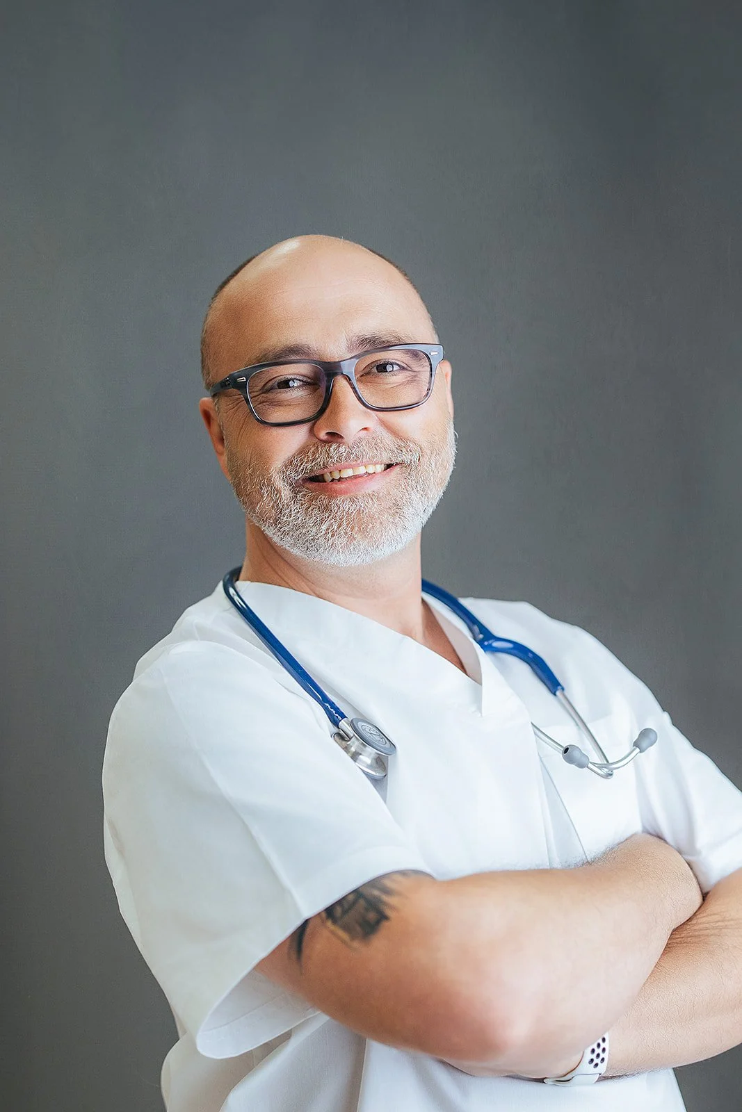 Durham Tech nursing student with glasses and arms crossed, warm smile in white scrubs and blue stethoscope, professional headshot in Durham NC