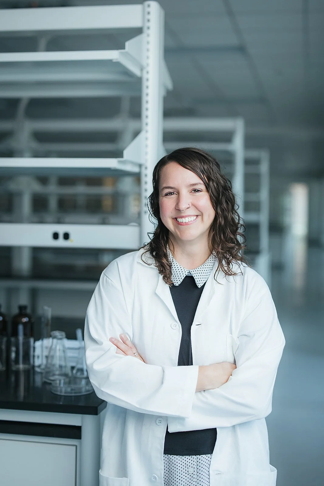 WomanCurlyBrownHairWhiteLabCoatArmsCrossedSmiling