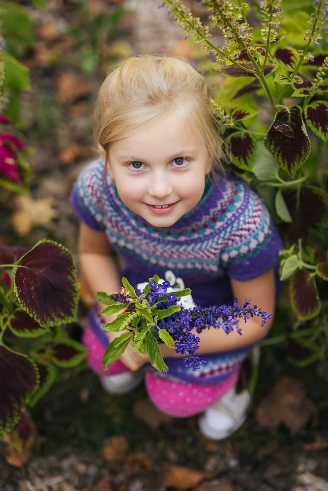 Daughter sitting in flowers with handful of picked flowers