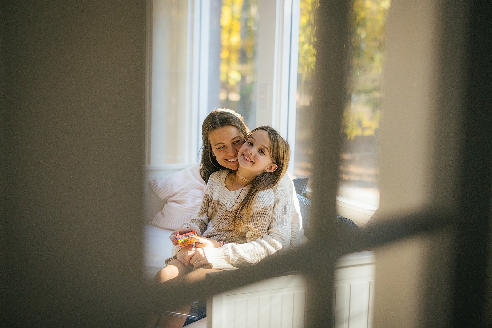 PhotoThroughWindowOfMomHuggingYoungDaughter