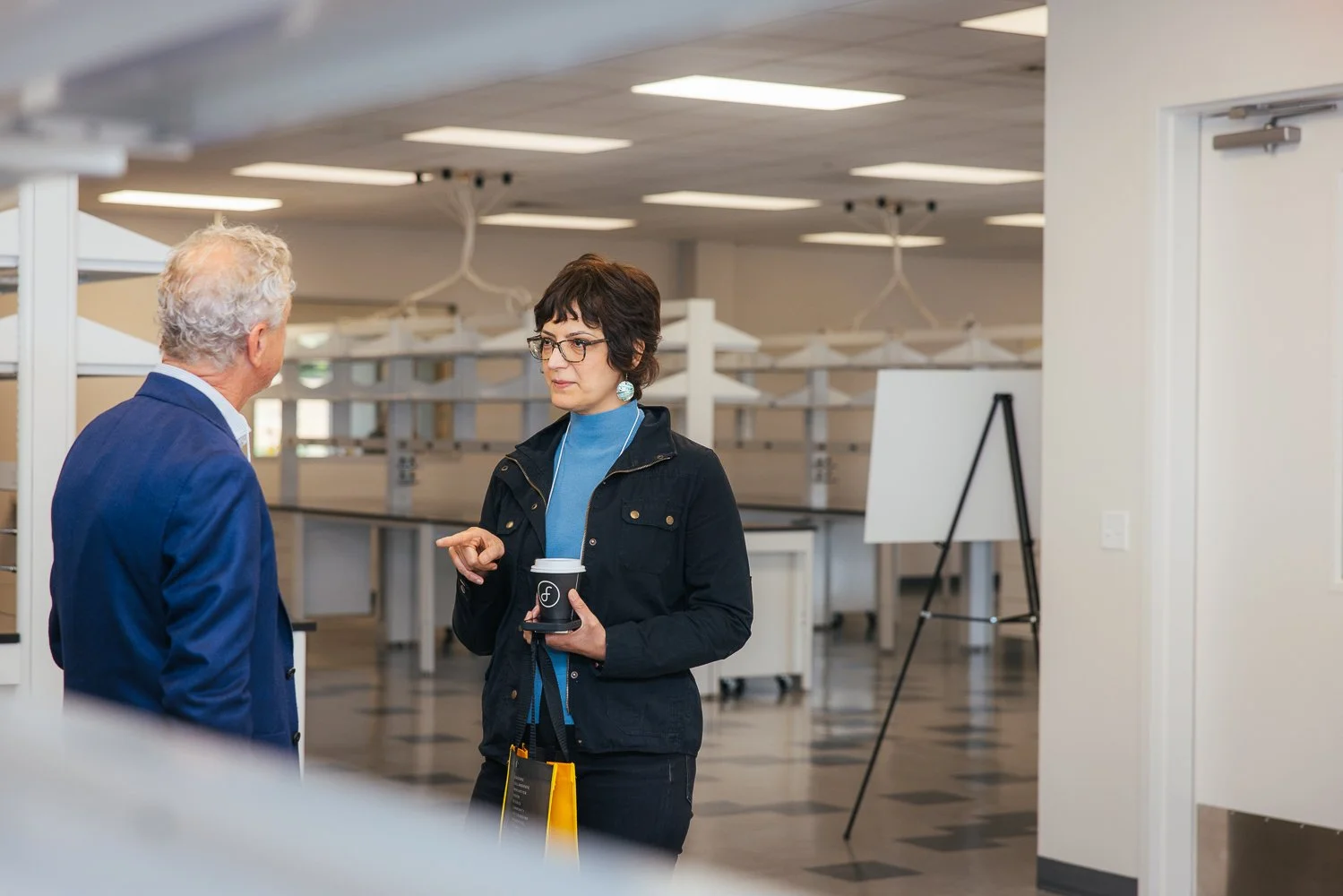 Woman with coffee gesturing in conversation near the lab space during a corporate event tour at Longfellow Triangle LIFE, Raleigh NC