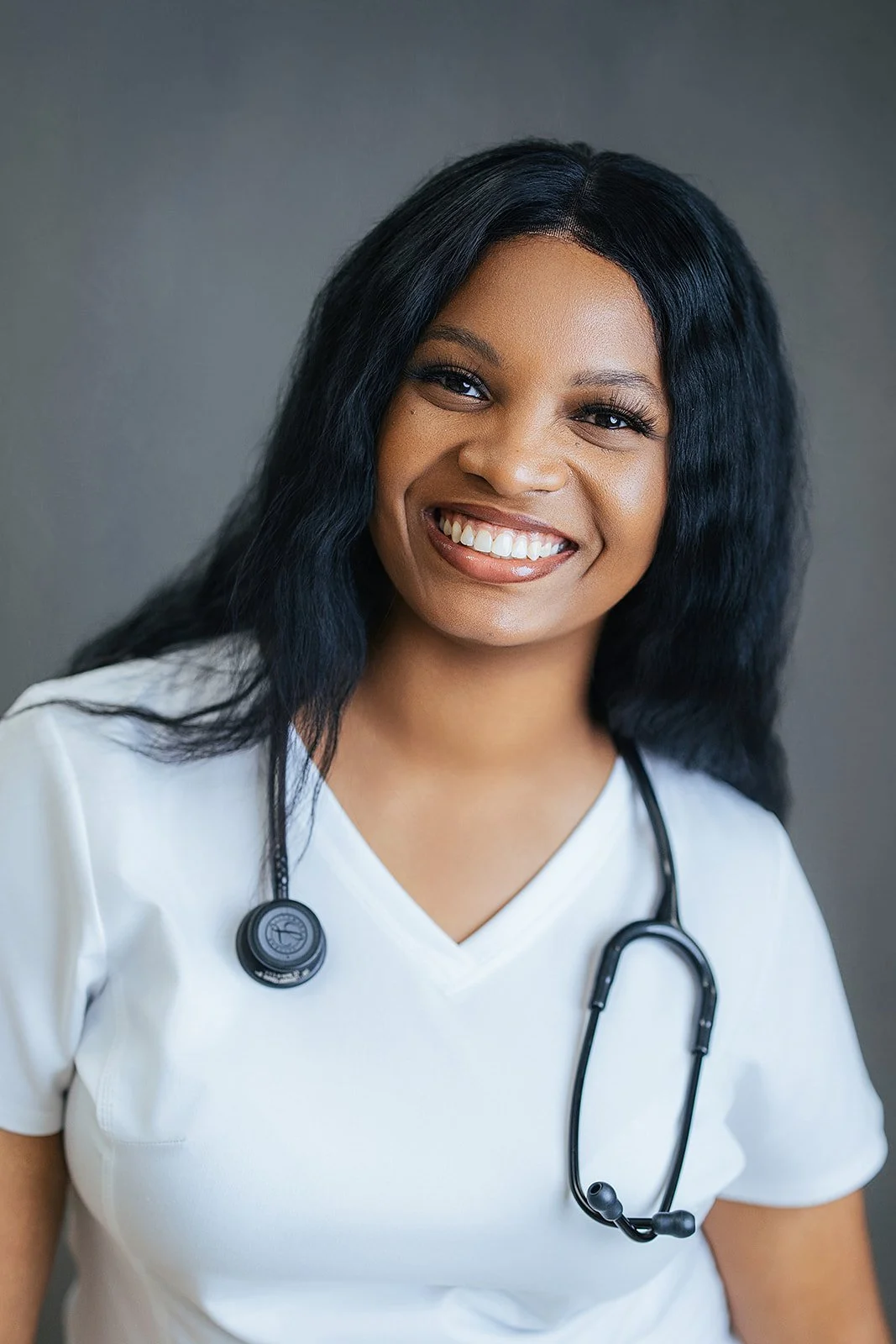 Durham Tech nursing student with long wavy black hair, radiant smile in white scrubs and black stethoscope, professional headshot in Durham NC