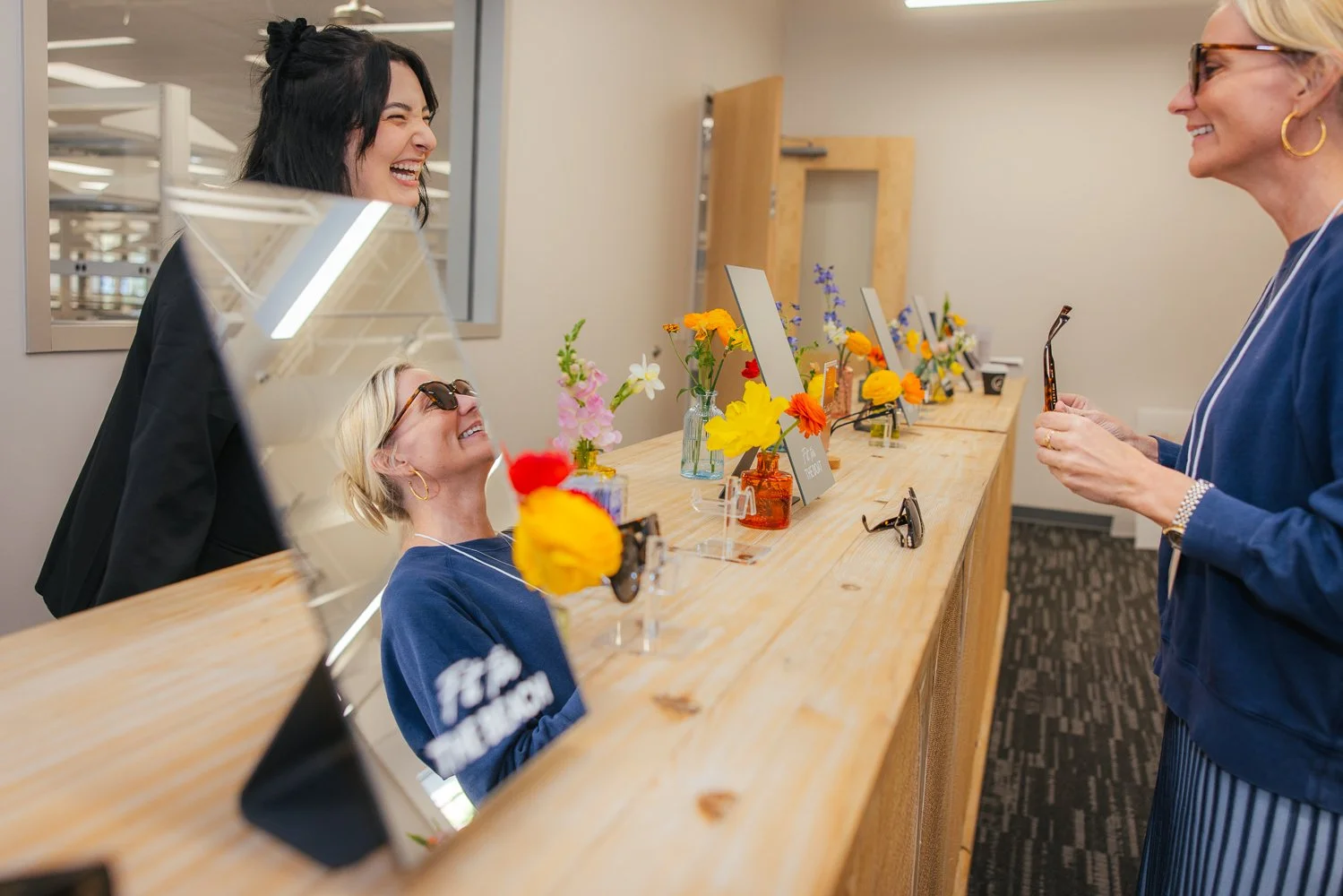Woman in white coat laughing while trying on sunglasses at a branded activity table at a corporate event at Longfellow Triangle LIFE in Raleigh NC