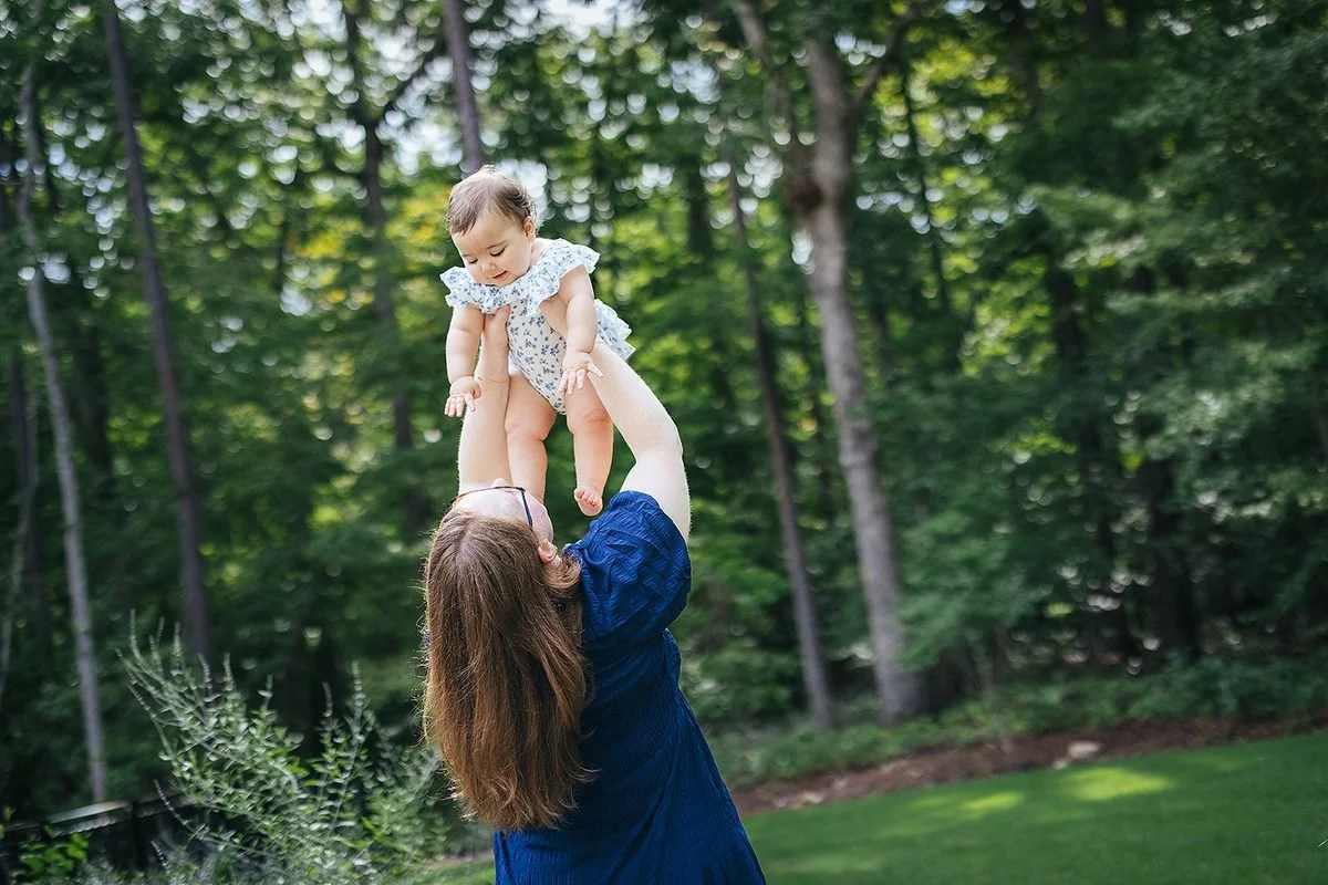 Mom holding baby girl up in air in the backyard