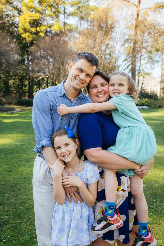 Family portrait of parents and two daughters laughing together on the green lawn at Duke Gardens in Durham North Carolina