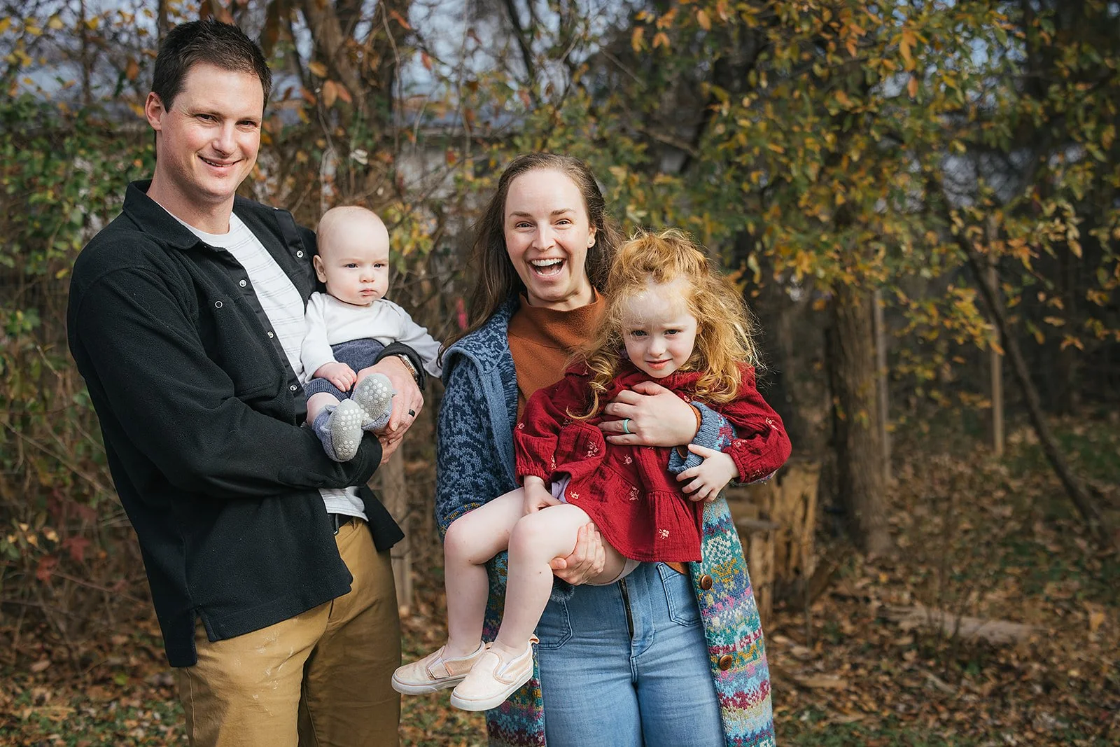 Happy family of four laughing together outdoors in fall foliage during Durham NC family photography session