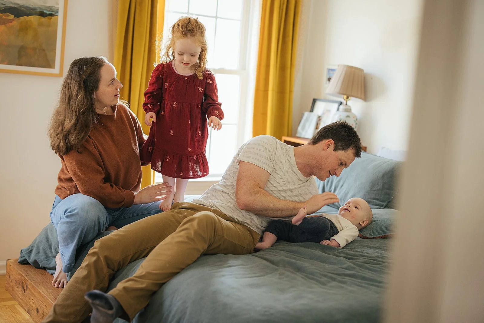 Family of four together in bedroom with beautiful morning window light during Durham lifestyle family photography session